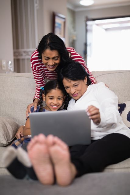 Multi-generation family sitting on couch, using laptop together. Perfect for themes of family bonding, technology in everyday life, and intergenerational relationships. Ideal for advertisements, family-oriented content, and articles about digital literacy and family dynamics.