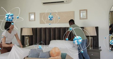 Couple making bed together in modern bedroom with tufted headboard and plush bear