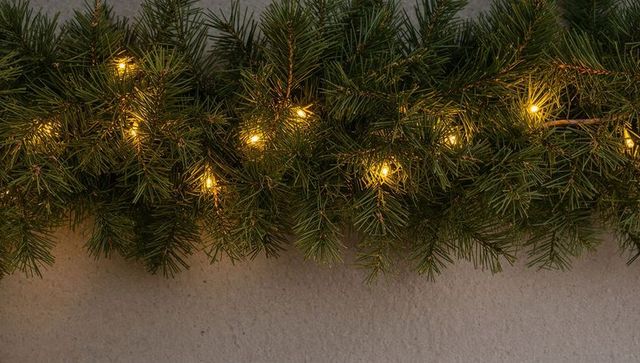 Glowing pine garland with warm white led lights on textured plaster wall for holiday decor