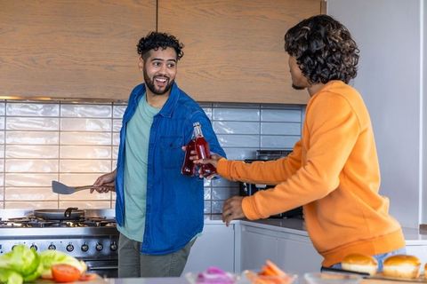 Friends cooking together in kitchen, sharing drinks and laughing as they prepare meal