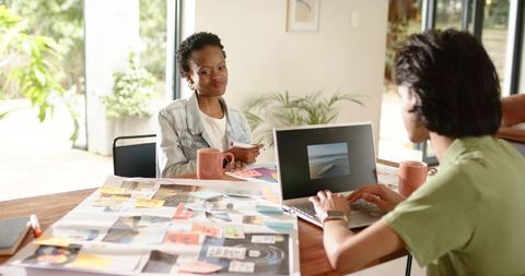 Diverse coworkers collaborating over moodboard and laptop in sunlit minimalist workspace