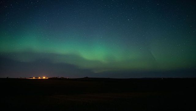 Glowing northern lights stretching across starry sky over prairie with warm horizon glow