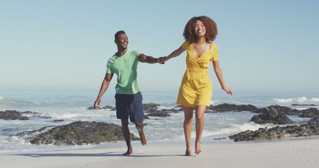 Smiling diverse couple holding hands and running on sunny beach by the sea. Summer, free time, relaxation, romance and vacations.