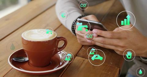 Tapping hands holding smartphone beside latte with ar sustainability analytics icons