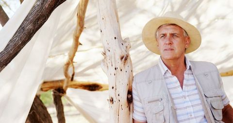 Thoughtful explorer in rustic outdoors with makeshift shelter