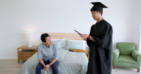 Young graduate showing diploma to proud father in home setting