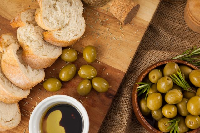 Rustic Mediterranean snack featuring sliced bread, green olives, and a bowl of olive oil with balsamic vinegar on a wooden cutting board. Ideal for use in food blogs, culinary websites, healthy eating promotions, and Mediterranean cuisine advertisements.