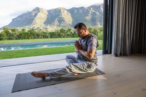 Man practicing seated yoga meditation by open glass door with pool and mountain view