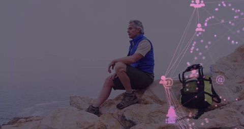 Man hiking sitting on rocky cliff overlooking ocean