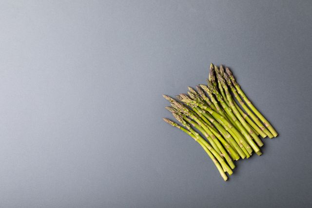 Fresh asparagus spears arranged on a gray background with ample copy space. Ideal for use in food blogs, healthy eating articles, nutrition websites, and organic produce promotions. The minimalist composition highlights the freshness and natural appeal of the asparagus, making it perfect for advertisements and culinary presentations.