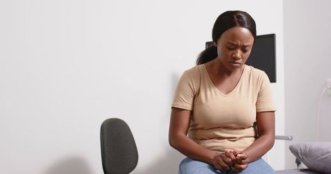 Worried patient sitting on exam bed clasping hands during clinical consultation