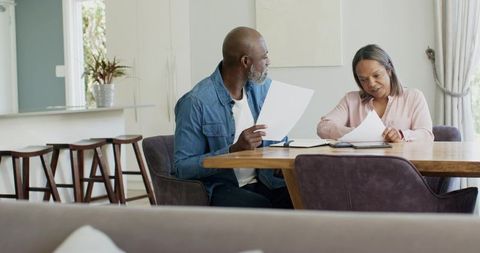 Couple reviewing financial documents at dining table planning budget managing bills