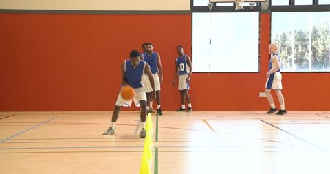 Young male basketball players practicing dribbling drills indoors