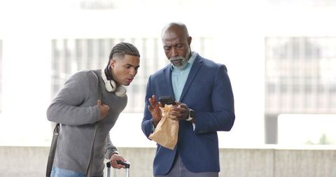 Business traveler and young commuter checking smartphone on urban transit platform