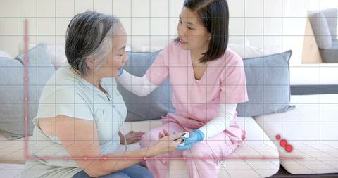 Caregiver checking blood glucose and comforting elder on sofa, pink scrubs, blue gloves