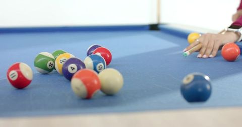 Female friends playing pool on blue-felt table aiming cue stick with billiard balls