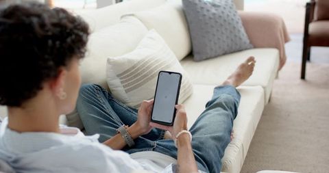 Young man reclining on sofa using smartphone at home casual denim lifestyle scene