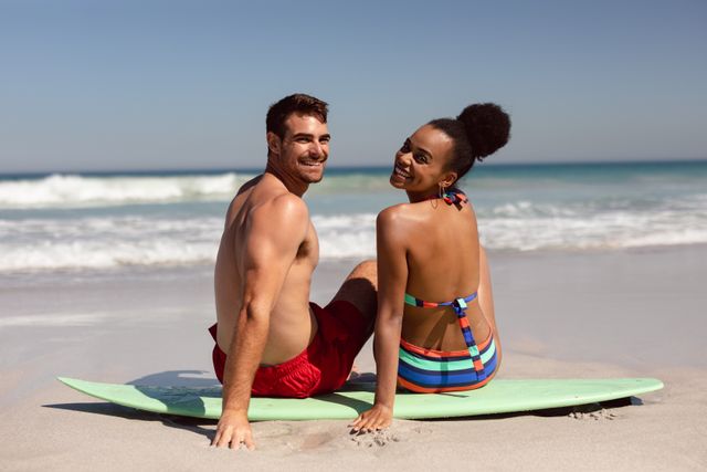 Young couple looking at camera while sitting on surfboard at beach in the sunshine - Download Free Stock Photos Pikwizard.com