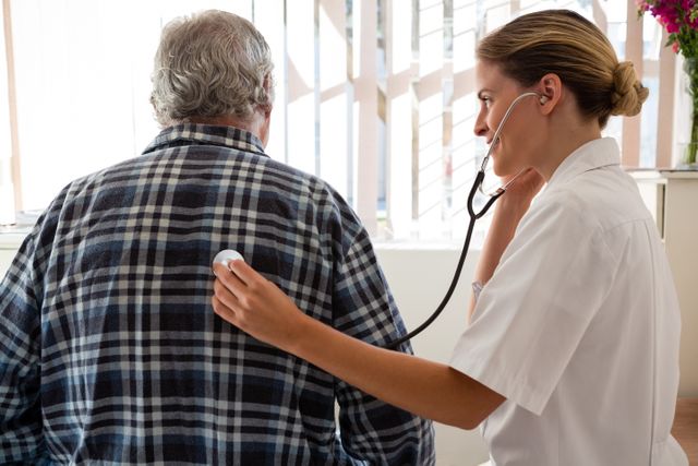 Side view of female doctor examining senior patient with stethoscope at nursing home