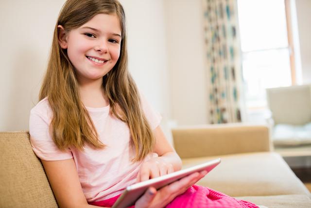Portrait of girl sitting on sofa using digital tablet in living room at home