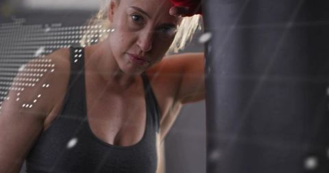 Leaning woman resting at punching bag after intense boxing session, focused determination