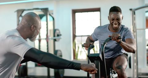 African American Trainer Coaching Athlete on Assault Bike During Intense Gym Workout