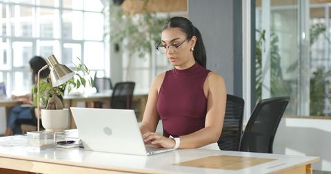 Indian professional woman typing on laptop in bright modern coworking office with plants