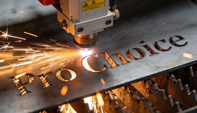 Cnc laser cutting pro choice text into steel plate producing bright sparks and precision finish