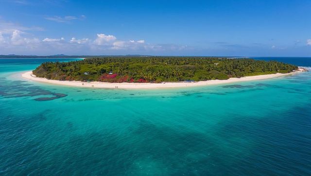 Aerial overlooking tropical islet with white sand beach and turquoise lagoon