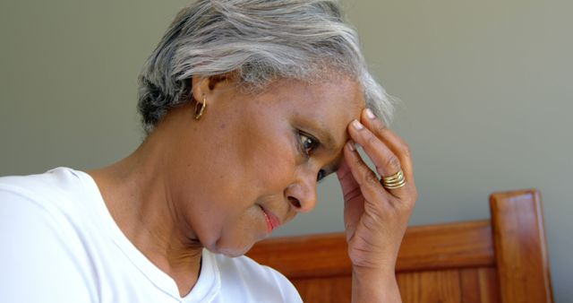 Elderly woman appears stressed and anxious while sitting at home. Useful for topics on mental health, aging, and personal stress.