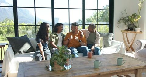 Friends sitting on sofa laughing and chatting in sunlit modern living room with coffee mugs