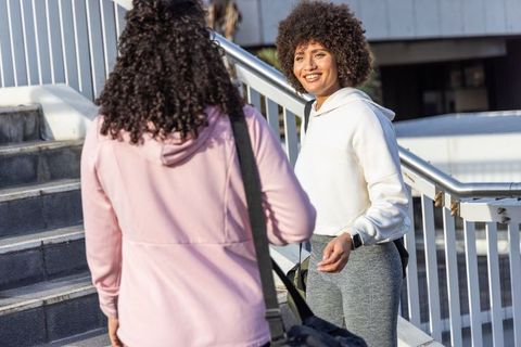 Two women chatting and smiling on urban stairs with backpacks and smartwatch