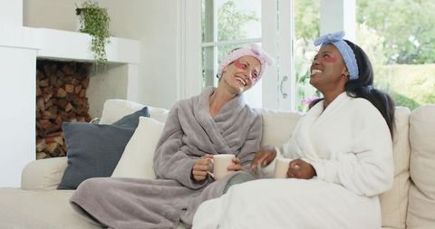 Diverse friends relaxing at home in cozy bathrobes with coffee