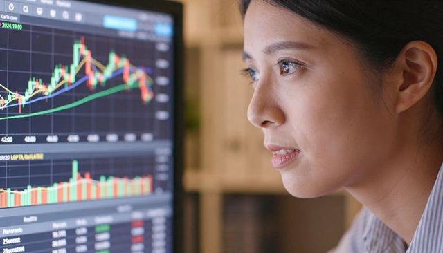 Asian woman analyzing candlestick charts on monitor for stock trading and market analytics