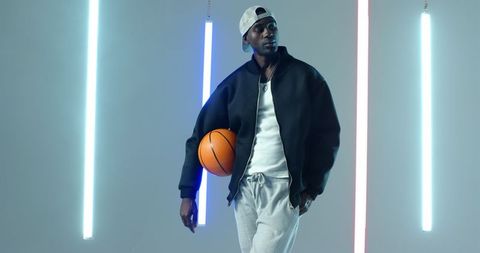 Stylish athlete holding basketball in futuristic studio setting