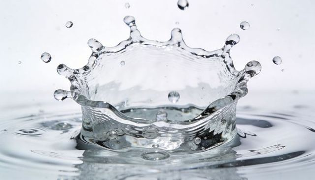 Crown splash creating crystal water halo with floating droplets and reflective ripples