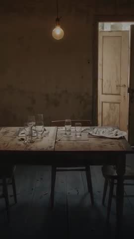 Vertical video of flickering bulb casting warm light over rustic wooden table with glassware