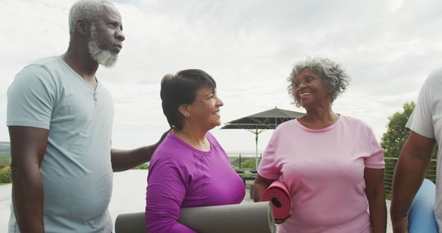 A diverse group of senior adults smiles and interacts outdoors holding yoga mats. This image is ideal for content promoting outdoor fitness activities, senior well-being, community programs, and multicultural health lifestyle solutions.