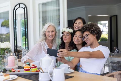 Multigenerational women taking selfie at sunlit brunch with tea and desserts