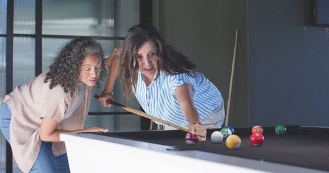 Women lining up precision pool shot in modern home game room showing focus and camaraderie