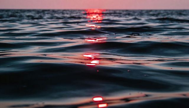 Rippling ocean surface with red sunset reflection trail and pink horizon glow
