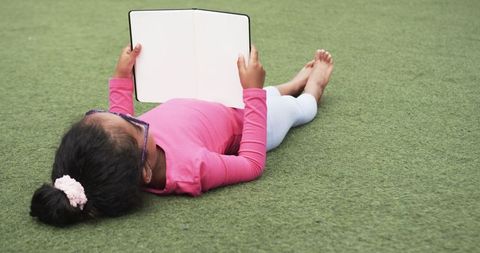 Young Girl Reading Outdoors on Green Grass in Relaxed Pose
