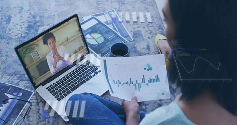 Remote team member reviewing financial charts during video call with laptop and printouts