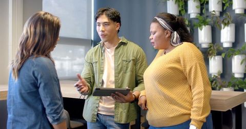 Diverse coworkers collaborating around tablet at modern office counter with greenery