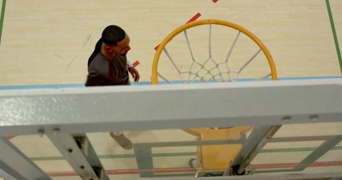 Overhead shot black male basketball player walking past hoop on indoor hardwood court