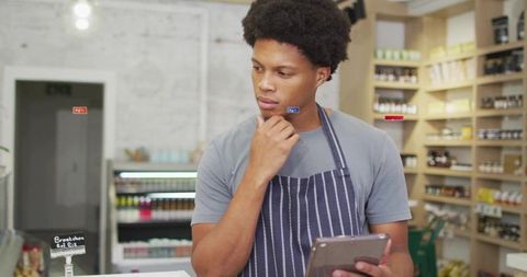 Grocery Employee Reviewing Tablet in Modern Deli with Striped Apron