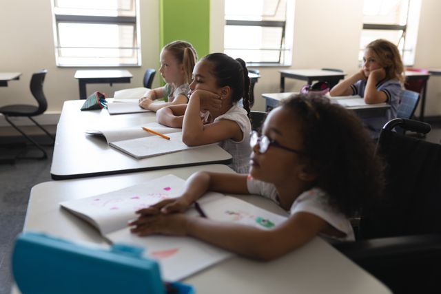 Children sitting at desks in an elementary school classroom, focused on their studies. Ideal for educational content, school advertisements, and articles on primary education. Highlights diversity and academic engagement among young students.