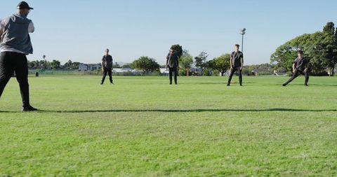 Diverse cricket team practicing fielding drill on sunny grass park building teamwork skills