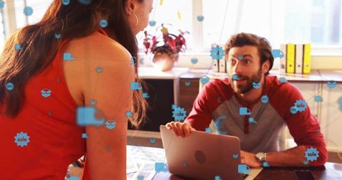 Colleagues collaborating over laptop with augmented reality sales icons in bright office