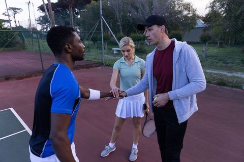 Diverse tennis players joining hands in pre-match huddle on outdoor red court